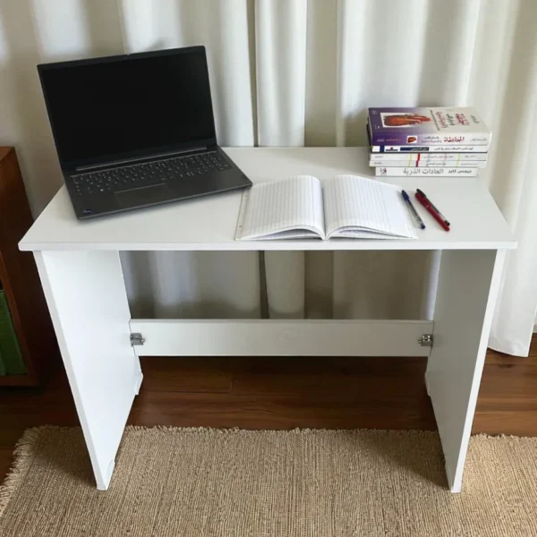 Vue de face d'un bureau démontable blanc, avec un ordinateur portable, un cahier et des stylos.
