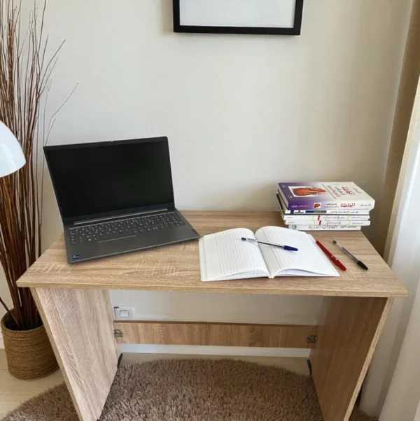 Un bureau démontable en bois clair, avec un ordinateur portable, des livres et des stylos.