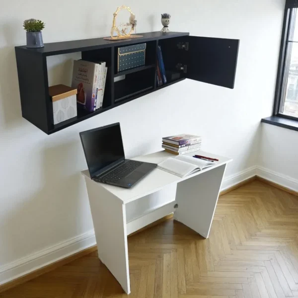 Un bureau pliant blanc avec un ordinateur portable, placé sous une étagère murale noire avec la porte ouverte.