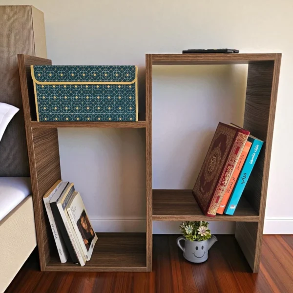 Table d'appoint en bois foncé utilisée comme table de chevet à côté d'un lit, avec des livres et une boîte de rangement sur ses étagères.