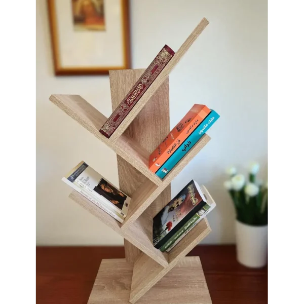 Meuble à livres asymétrique en bois clair posé sur une table, avec un tableau et une plante en arrière-plan.