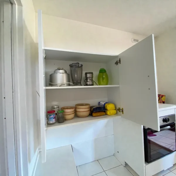 Intérieur d'un meuble de rangement mural blanc avec tablette, contenant un mixeur, des bols et des fournitures.