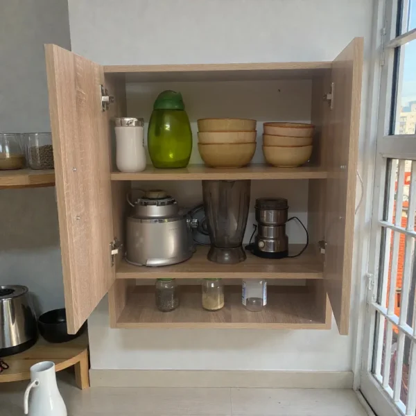 Intérieur d'un caisson de rangement mural bois avec étagère centrale, utilisé pour stocker des robots de cuisine et des bocaux.