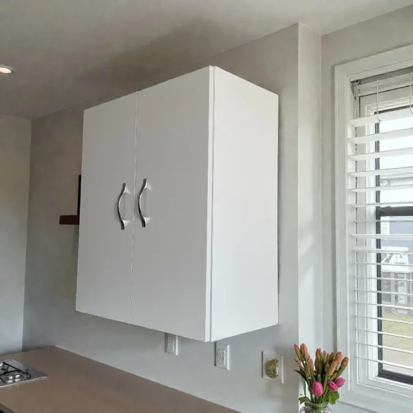 Vue en angle d'un caisson de cuisine blanc, deux portes, installé au-dessus d'un plan de travail en bois. Meuble d'appoint compact idéal pour un rangement additionnel en cuisine ou dans un garage.