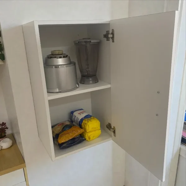 Élément haut cuisine blanc porte ouverte avec robot mixeur et paquets de nourriture sur l'étagère.