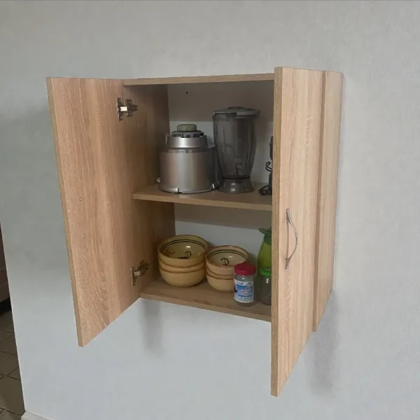 Gros plan sur l'intérieur d'une armoire de cuisine murale ouverte, comprenant deux étagères. L'étagère supérieure contient des appareils de petit électroménager (mixeur et blender). L'étagère inférieure contient des bols et des ustensiles.