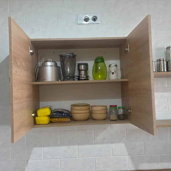 Intérieur d'un placard mural imitation chêne clair avec vaisselle et robots de cuisine bien organisés.