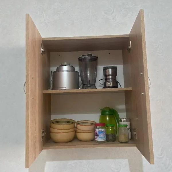 Meuble haut de cuisine deux portes ouvert. L'intérieur révèle un rangement pratique avec deux étagères. On y voit un mixeur, un moulin à café, des bols de service, des épices et des bocaux. La couleur est chêne clair.