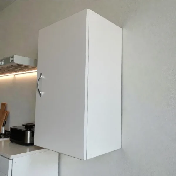 Vue de côté d'un placard mural blanc fermé installé au-dessus du plan de travail.
