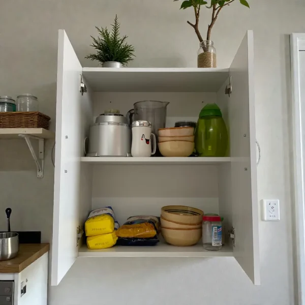 Meuble haut cuisine blanc ouvert, montrant deux étagères intérieures remplies. Rangement organisé pour petit électroménager (mixeur), bols de vaisselle, épicerie et sacs de farine.