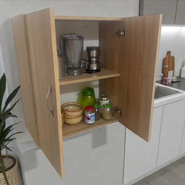 Armoire de cuisine murale ouverte révélant le rangement intérieur. Sur l'étagère supérieure, un mixeur et un blender. Sur l'étagère inférieure, des bols, des bocaux et une gourde. Vue en angle montrant l'aménagement sous l'armoire.