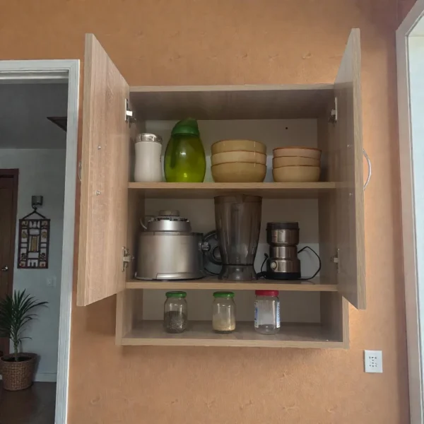 Armoire murale ouverte avec tablette intérieure montrant le rangement de vaisselle, bols et petit électroménager.