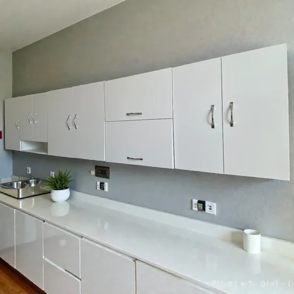 Vue d'une cuisine moderne avec un ensemble complet de meubles hauts blancs, incluant un élément avec niche et des placards basculants, au-dessus d'un plan de travail blanc.